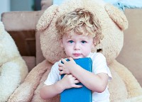 Portrait of an adorable little boy reading with his teddy bear at home